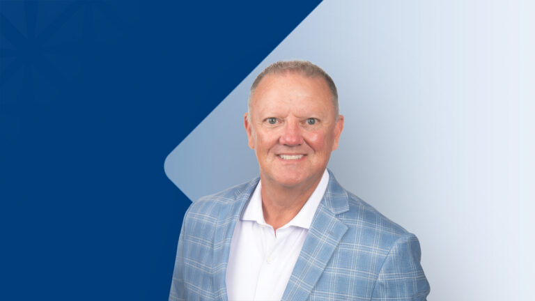 Professional headshot of a smiling man in a light blue plaid blazer and white shirt, set against a dark blue diagonal banner and pale gradient background (corporate profile image).